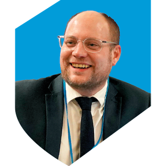 Man wearing a suit and glasses with a light blue shield in the background