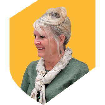 Woman with blonde hair in a green top with a white scarf sitting with a yellow background in the shape of a shield.