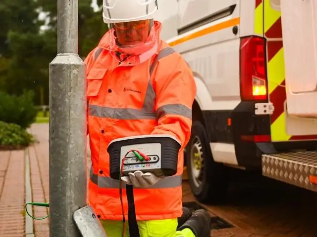 A man in high visability clothing checking the electrical flow of a street lamp.