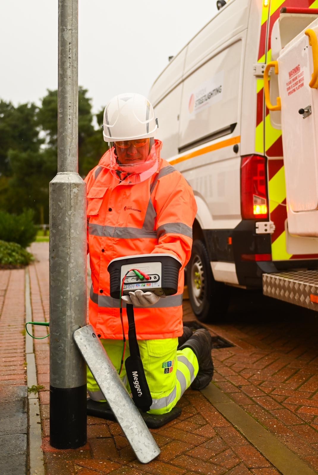 A man in high visability clothing checking the electrical flow of a street lamp. 